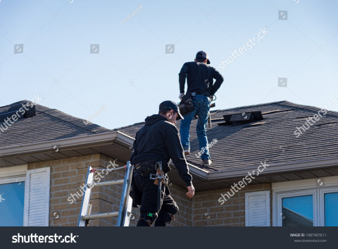 Stock photo two roofers inspecting a damaged roof 1087407611